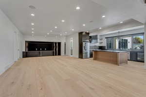 Kitchen featuring open floor plan, a kitchen island, open shelves, high end fridge, and dark countertops
