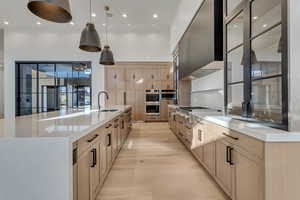 Kitchen with light stone countertops, hanging light fixtures, range hood, stainless steel appliances, and two tone cabinets