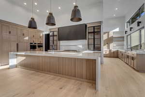 Kitchen featuring a high ceiling, light wood-type flooring, light stone countertops, pendant lighting, and two tone color scheme