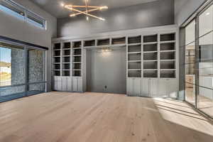Unfurnished living room with wood-type flooring, a chandelier, a high ceiling, and built in shelves