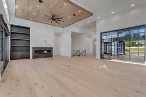 Unfurnished living room with built in shelves, a fireplace, light wood finished floors, a ceiling fan, and recessed lighting