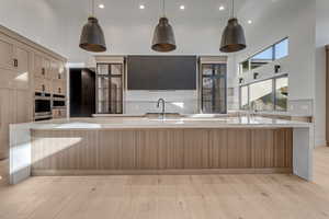 Kitchen with a high ceiling, a large island with sink, light wood-style flooring, light stone counters, and two tone color scheme
