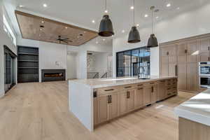 Kitchen with built in features, open floor plan, a large fireplace, a high ceiling, and light wood-style floors