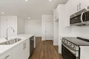 Kitchen featuring stainless steel appliances, white cabinets, dark wood finished floors, light stone counters, and recessed lighting