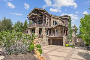 View of front of house with stone siding, concrete driveway, an attached garage, a standing seam roof, and a balcony