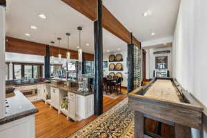 Kitchen featuring white cabinets, light wood-type flooring, dark stone countertops, decorative light fixtures, and beam ceiling
