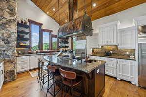 Two tone kitchen featuring a vaulted wooden ceiling, decorative backsplash, dark stone countertops, light wood-style floors, and a breakfast bar