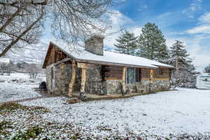 Snow covered property featuring stone siding, a chimney, and log siding