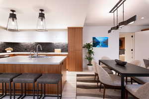 Two tone kitchen featuring modern cabinets, a breakfast bar, hanging light fixtures, light wood finished floors, and decorative backsplash
