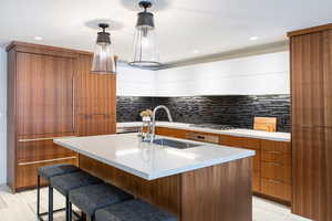 Dual tone kitchen featuring modern cabinets, a kitchen island with sink, light stone countertops, decorative backsplash, and a kitchen bar