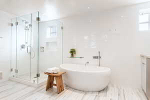 Bathroom featuring a stall shower, a soaking tub, healthy amount of natural light, tile walls, and vanity