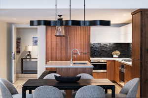 Two tone kitchen featuring modern cabinets, stainless steel appliances, a kitchen island with sink, dual tone cabinets, and tasteful backsplash