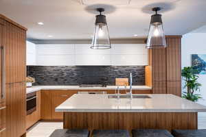 Dual tone kitchen with modern cabinets, a breakfast bar area, dual tone cabinets, a kitchen island with sink, and decorative backsplash