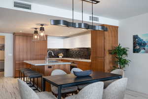 Kitchen with modern cabinets, two tone cabinetry, hanging light fixtures, an island with sink, and stainless steel appliances