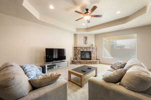 Living room featuring a raised ceiling, ceiling fan, light carpet, a fireplace, and recessed lighting