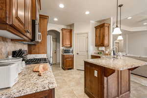 Kitchen featuring wood finish cabinetry, a peninsula, light stone counters, arched walkways, and gas range oven