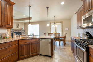 Kitchen with tasteful backsplash, a peninsula, light stone countertops, stainless steel appliances, and wood finish cabinetry