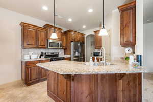 Kitchen with arched walkways, a peninsula, wood finish cabinets, stainless steel appliances, and light stone countertops
