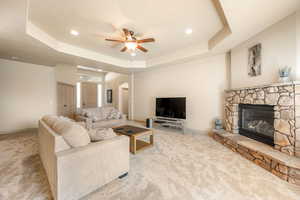 Living room featuring ceiling fan, arched walkways, light carpet, a fireplace, and a raised ceiling