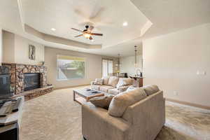 Carpeted living area with ceiling fan, a fireplace, a raised ceiling, a textured ceiling, and recessed lighting