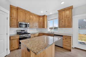 Kitchen with stainless steel appliances, light stone counters, backsplash, light wood-style floors, and a kitchen island