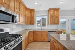 Kitchen featuring stainless steel appliances, light stone counters, light wood finished floors, backsplash, and recessed lighting
