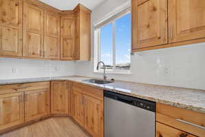 Kitchen with light stone countertops, stainless steel dishwasher, light wood finished floors, and decorative backsplash