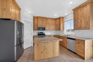 Kitchen with stainless steel appliances, light wood-style floors, light stone counters, decorative backsplash, and recessed lighting