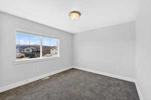 Unfurnished room featuring baseboards and dark carpet