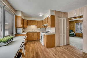 Kitchen featuring light countertops, white range with gas cooktop, a textured ceiling, light wood-style floors, and wooden walls