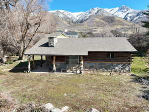 View of front facade with a mountain view, a front lawn, log siding, a chimney, and roof with shingles