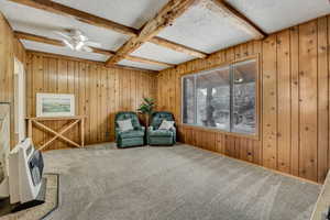 Living area featuring wood walls, beam ceiling, a textured ceiling, heating unit, and carpet