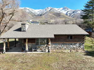 View of front of property with a mountain view, a chimney, a front lawn, log siding, and roof with shingles