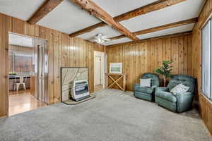 Sitting room with a textured ceiling, wood walls, carpet, beam ceiling, and a ceiling fan