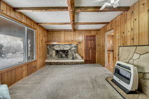 Unfurnished living room with wood walls, heating unit, carpet floors, a fireplace, and beamed ceiling