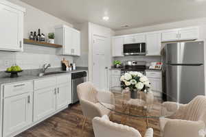 Kitchen with stainless steel appliances, white cabinets, dark wood-style floors, open shelves, and tasteful backsplash