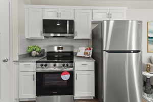 Kitchen with stainless steel appliances, white cabinetry, light stone countertops, and decorative backsplash