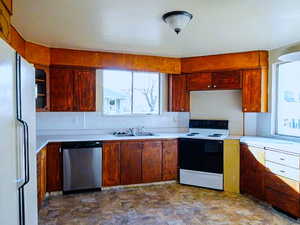 Kitchen with electric range oven, freestanding refrigerator, stainless steel dishwasher, and light countertops