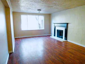 Unfurnished living room featuring dark wood-style floors, a glass covered fireplace, and a textured ceiling