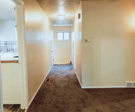 Corridor with dark colored carpet and a textured ceiling