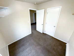 Unfurnished bedroom featuring dark carpet and baseboards