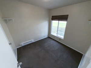 Unfurnished room featuring dark carpet and a baseboard heating unit