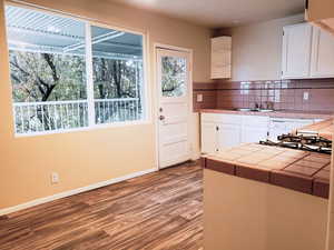 Kitchen featuring white cabinetry, dark wood finished floors, tile counters, decorative backsplash, and white appliances
