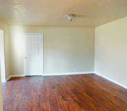 Empty room featuring dark wood-style flooring and a textured ceiling