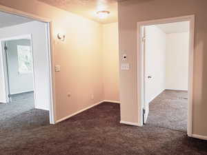 Hallway with dark colored carpet and a textured ceiling
