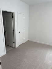 Unfurnished bedroom with light colored carpet and baseboards