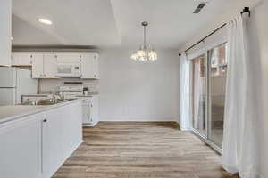 Kitchen featuring white cabinetry, a chandelier, white appliances, and light countertops