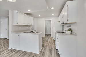 Kitchen with light countertops, white cabinets, white appliances, a peninsula, and recessed lighting