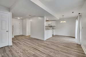 Unfurnished living room featuring suspended lighting and light wood-style floors
