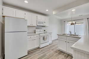 Kitchen with white appliances, white cabinets, light countertops, light wood-style floors, and hanging lights